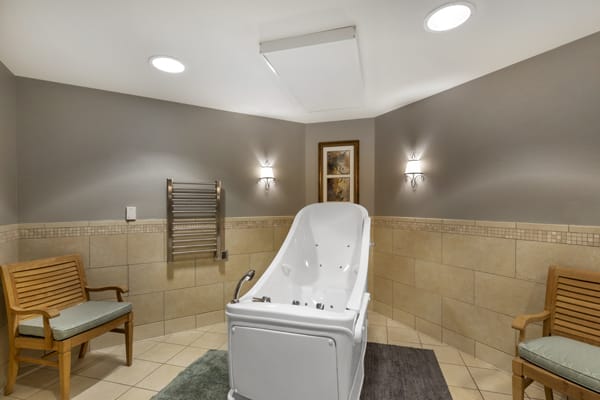 A modern bathroom featuring a walk-in tub with wall lights and tiled flooring.