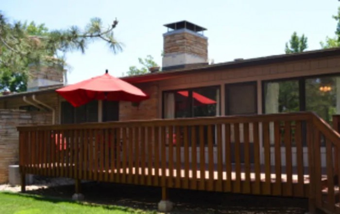 A house with a wooden deck featuring a red umbrella and a chimney.