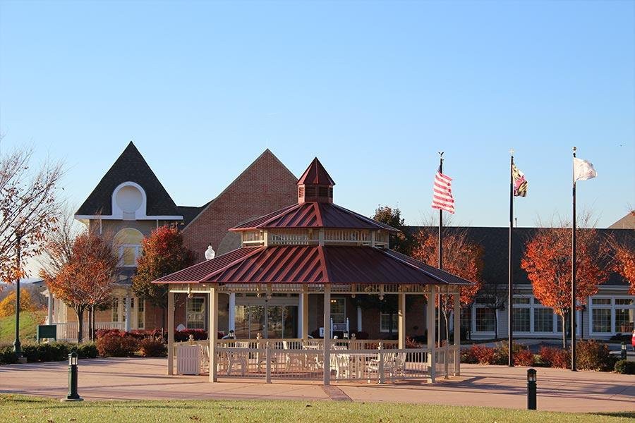 A gazebo in a park setting with flags and buildings in the background, under a clear blue sky.