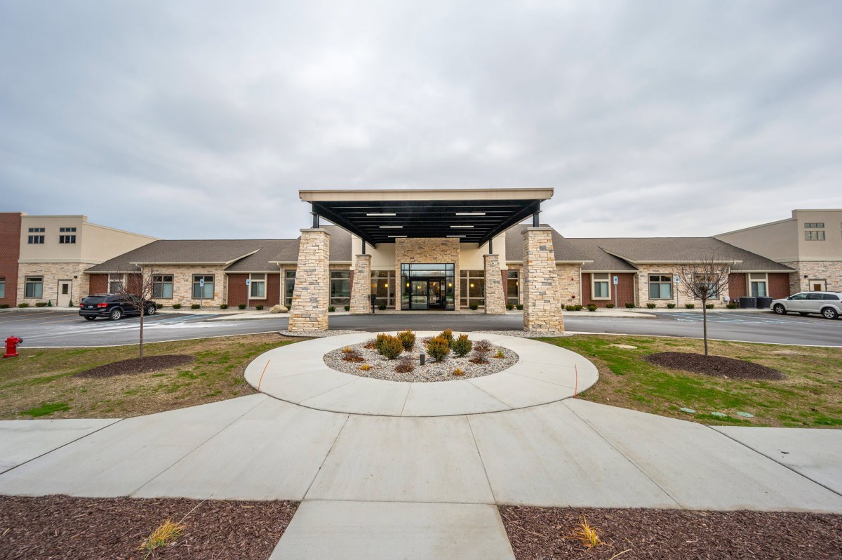 A modern building entrance with a circular driveway and landscaped surroundings under a cloudy sky.