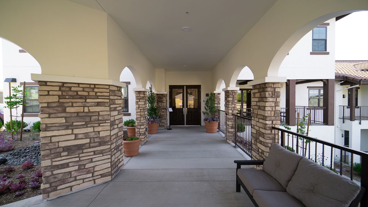 A covered entrance corridor with stone pillars, potted plants, and a bench.