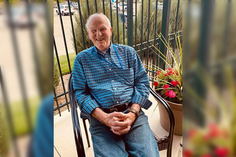 A man sitting on a patio, smiling and wearing casual clothing.