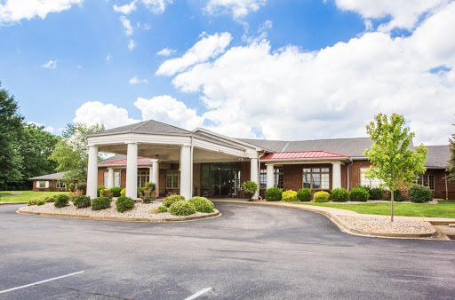 A welcoming hotel entrance surrounded by well-maintained landscaping under a bright, cloudy sky.