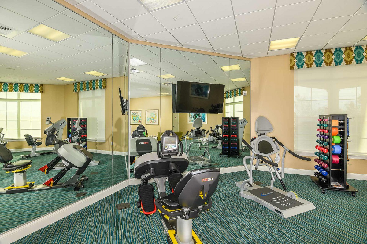 A well-equipped gym room featuring a stationary bike, treadmill, and large mirrors.