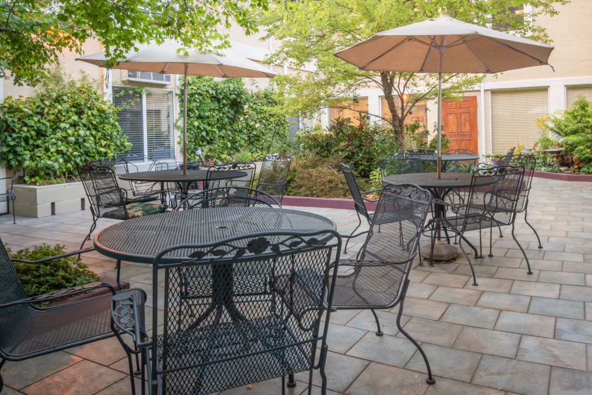 Cozy outdoor patio with iron tables, chairs, and umbrellas surrounded by greenery.