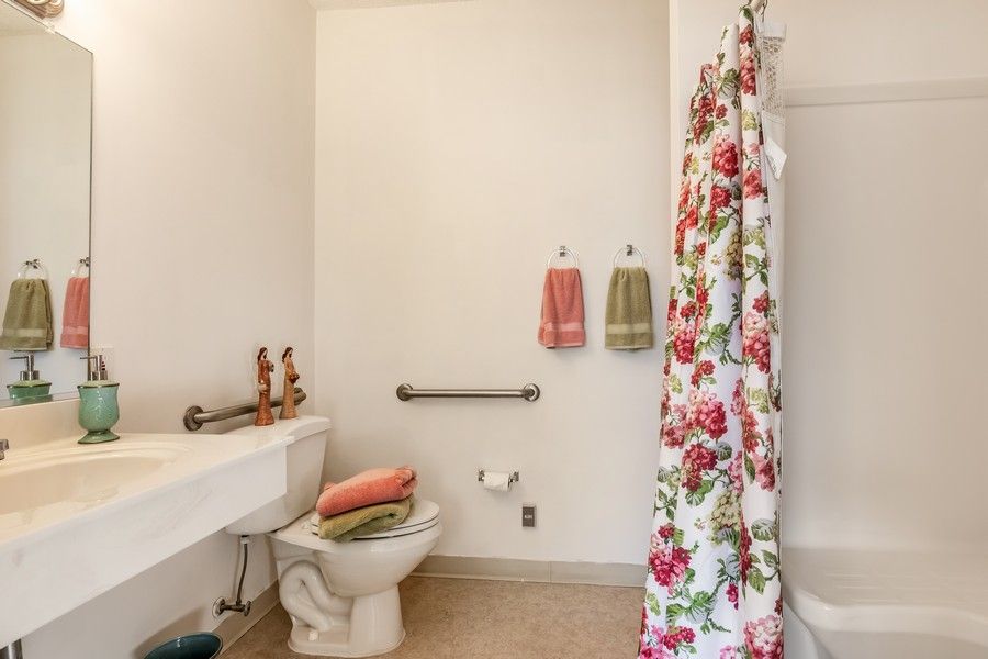 A bathroom featuring a floral shower curtain, towels on the wall, and a toilet with decor.