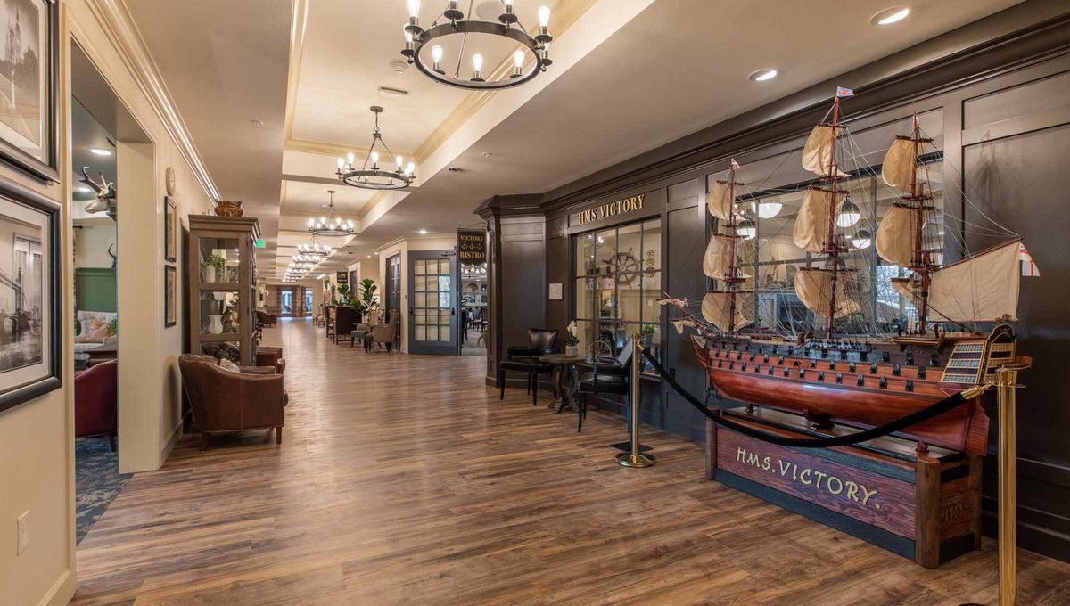 A spacious hotel lobby with chandeliers, wooden flooring, and a model ship display.