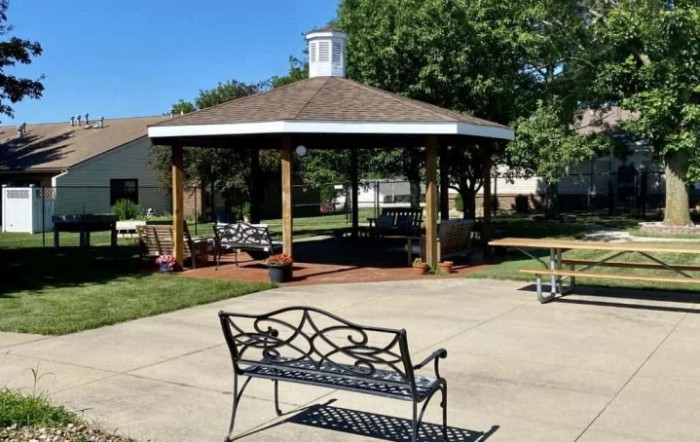 A gazebo with a nearby bench in a sunny outdoor setting.