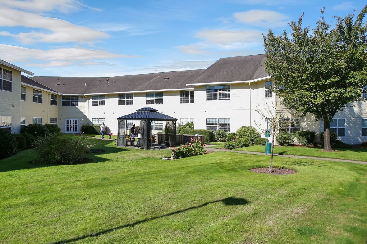 A scenic view of a residential building with a well-maintained lawn and gazebo under a clear blue sky.