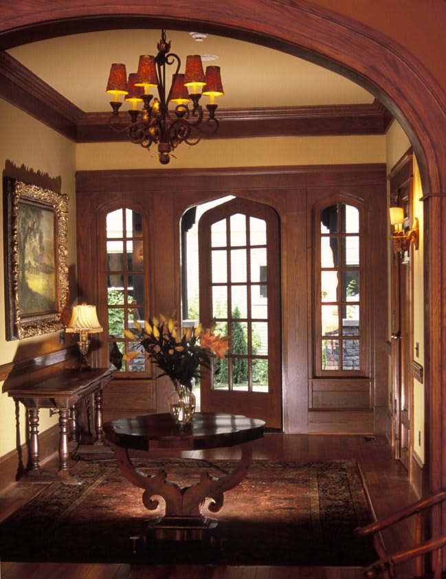 A traditional entryway featuring rich wood paneling, an arched doorway, and elegant decor with a central table and flower arrangement.