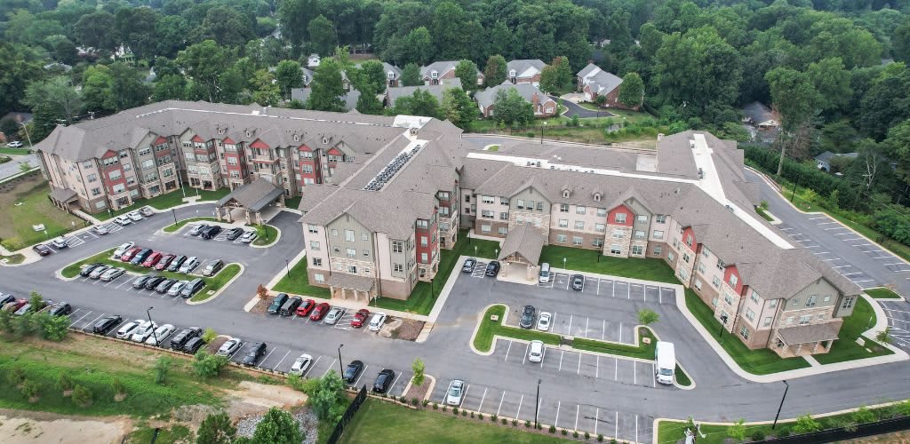 Aerial view of a residential building complex with adjacent parking lots and surrounding greenery.