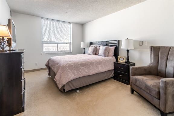 A cozy bedroom with a neatly made bed, bedside tables with lamps, and a window letting in natural light.