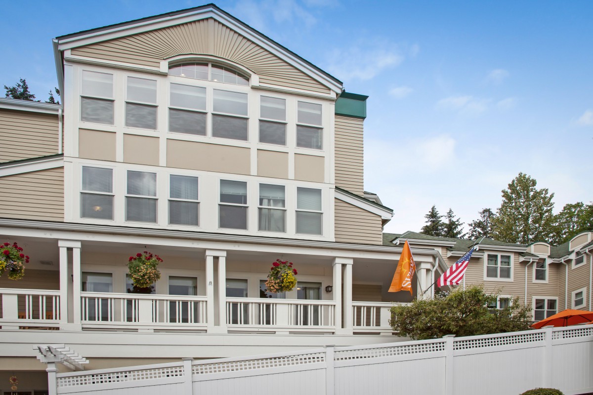 A multi-story residential building with a balcony, displaying flags and surrounded by a fence.
