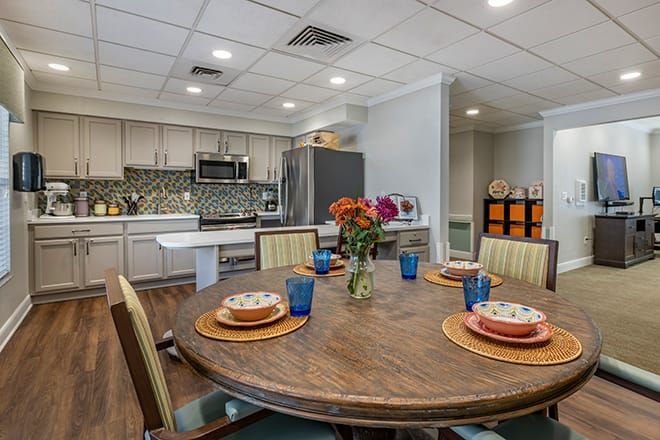 A modern kitchen and dining area featuring a round wooden table with colorful place settings and a vase of flowers.