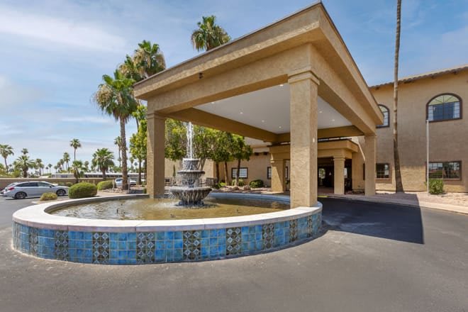 Hotel entrance with a decorative fountain and palm trees.