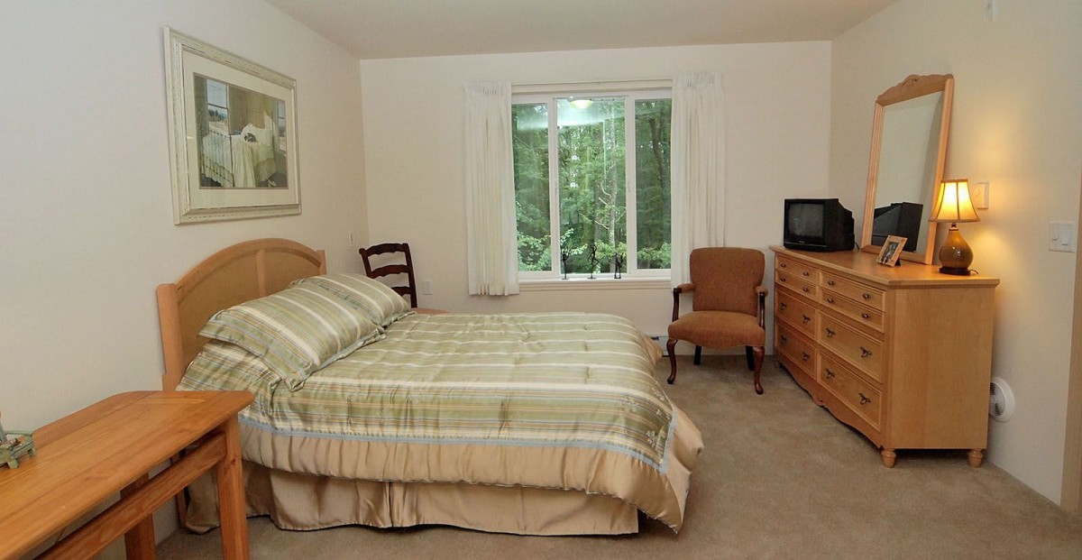 A cozy bedroom with a double bed, chairs, and a window overlooking greenery.