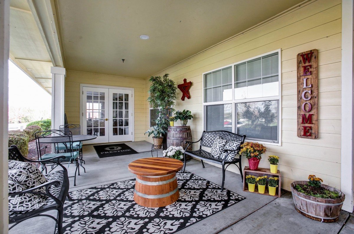 A cozy patio area featuring outdoor seating, a central table, decorative rug, and potted plants against a yellow wall.