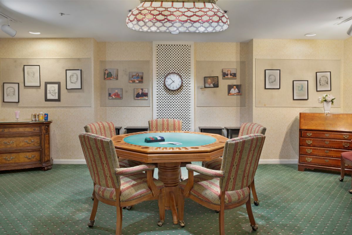 A stylish game room featuring a poker table surrounded by chairs, with playing cards set on the table and illuminated by an elegant chandelier.
