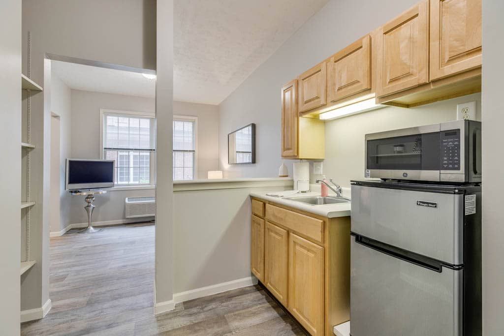 A cozy apartment kitchen with wooden cabinets, adjacent to a living room area.