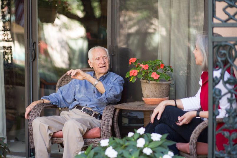 Two people having a conversation on a patio with flowers around.