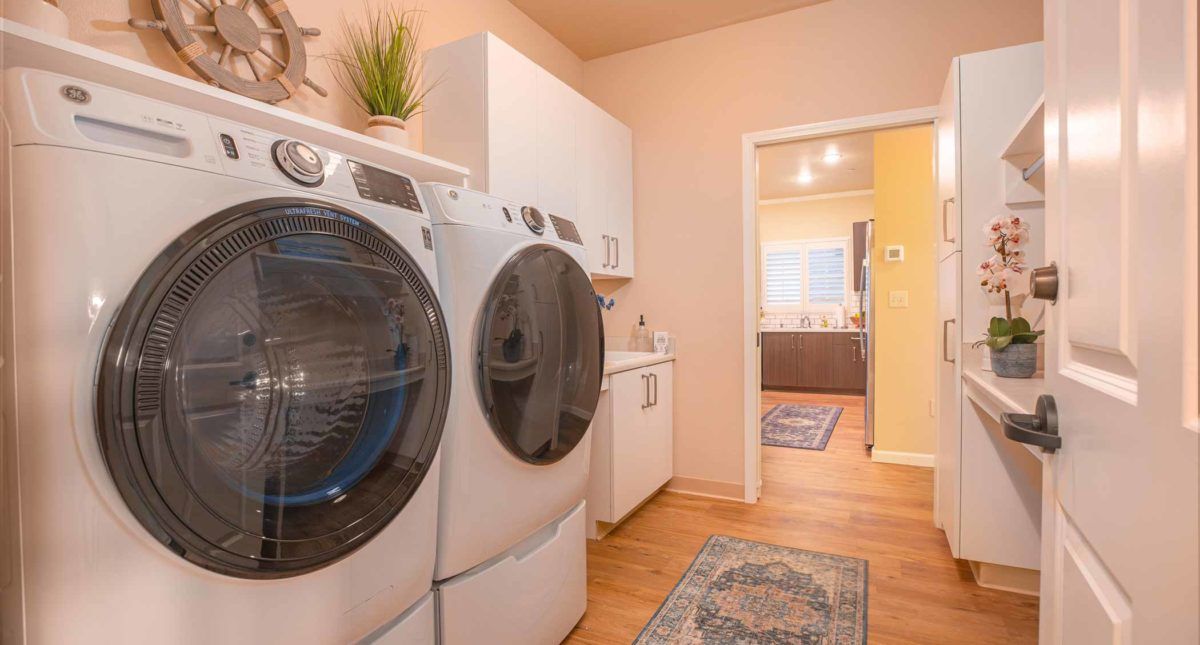 A well-organized laundry room featuring a washer and dryer with cabinetry and wood flooring.