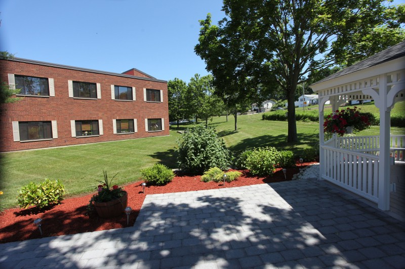 A landscaped garden area with a red-brick building in the background under a clear blue sky.