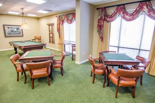 A cozy room with tables and chairs set up for gatherings, featuring green carpeting and natural light.