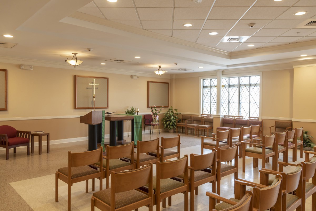 A serene chapel interior with rows of wooden chairs facing an altar.