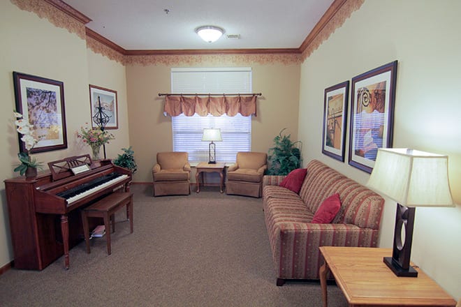 A cozy living room featuring a striped sofa, two armchairs, and a piano, with framed art on the walls.