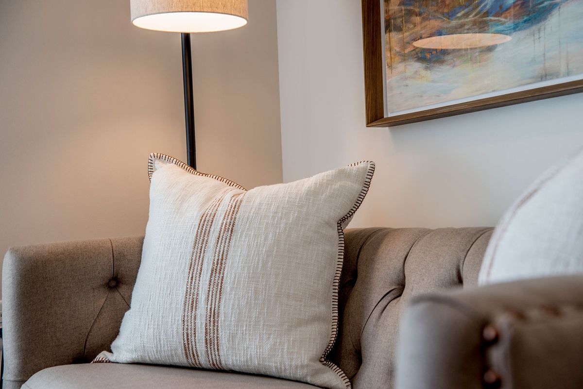 A cozy living room corner featuring a tufted sofa adorned with a decorative pillow, accompanied by a standing lamp and wall art.
