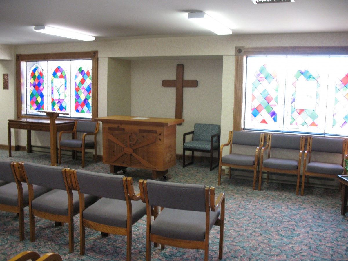 A small chapel with wooden chairs, a pulpit, and stained glass windows.