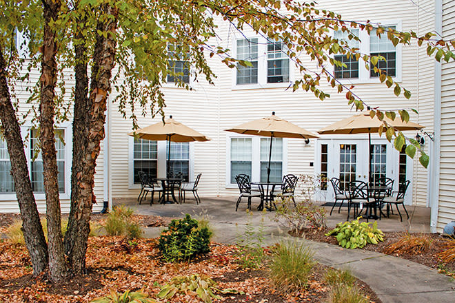 A cozy outdoor patio area with tables, chairs, and umbrellas set against a building backdrop.