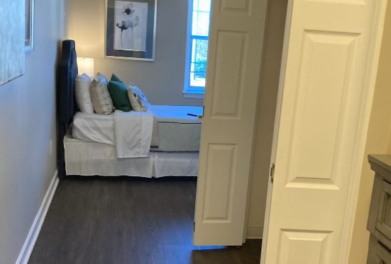 A cozy bedroom viewed through an open door, featuring a neatly made bed and decorative pillows.