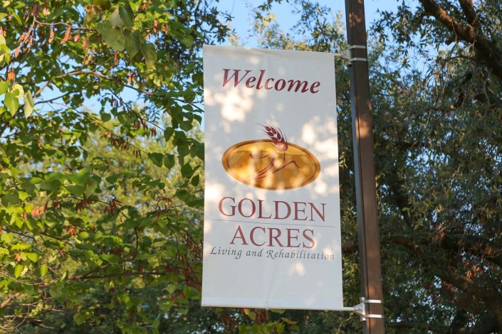 A welcome sign for Golden Acres hangs surrounded by autumn foliage.