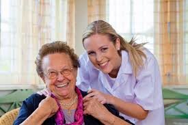 A caregiver poses happily with an elderly woman, both smiling warmly.