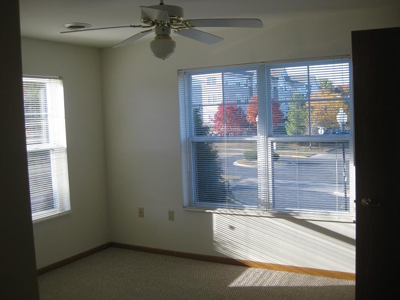 A bright, empty room with large windows and a ceiling fan.