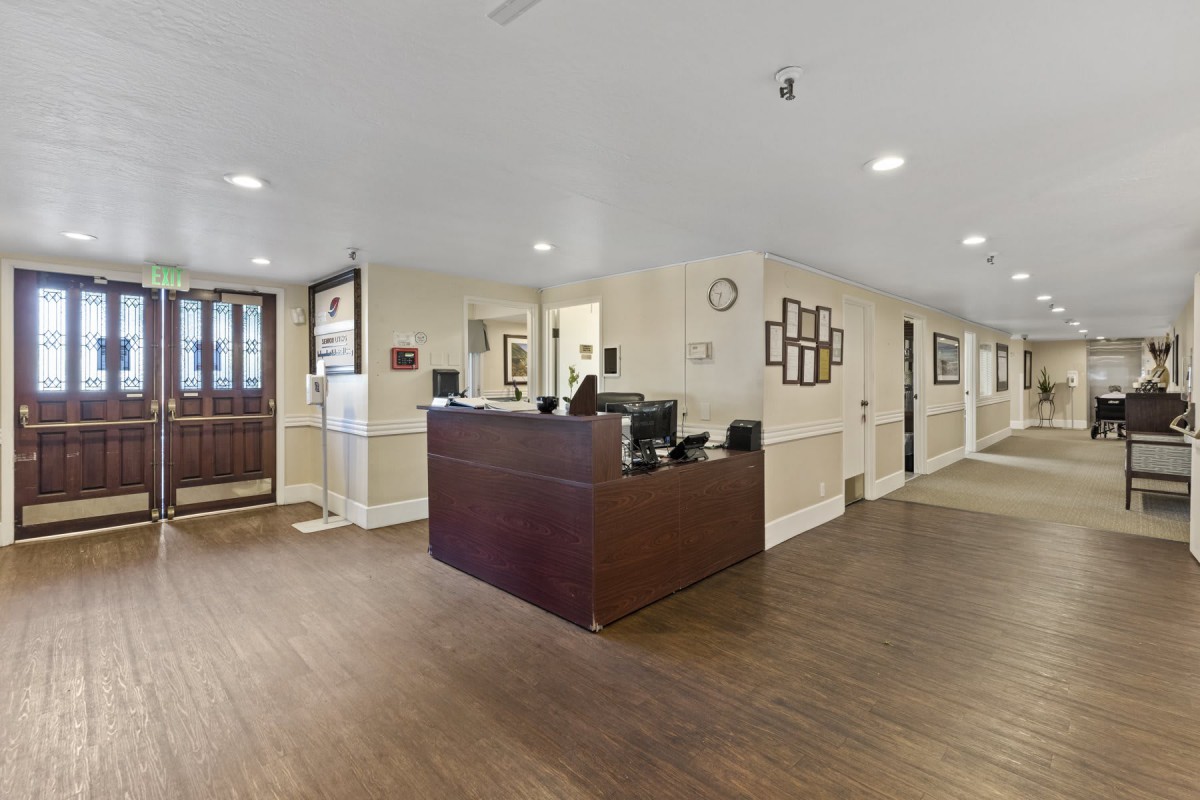 A spacious reception area with a wooden desk and floors, featuring office equipment and wall decor.