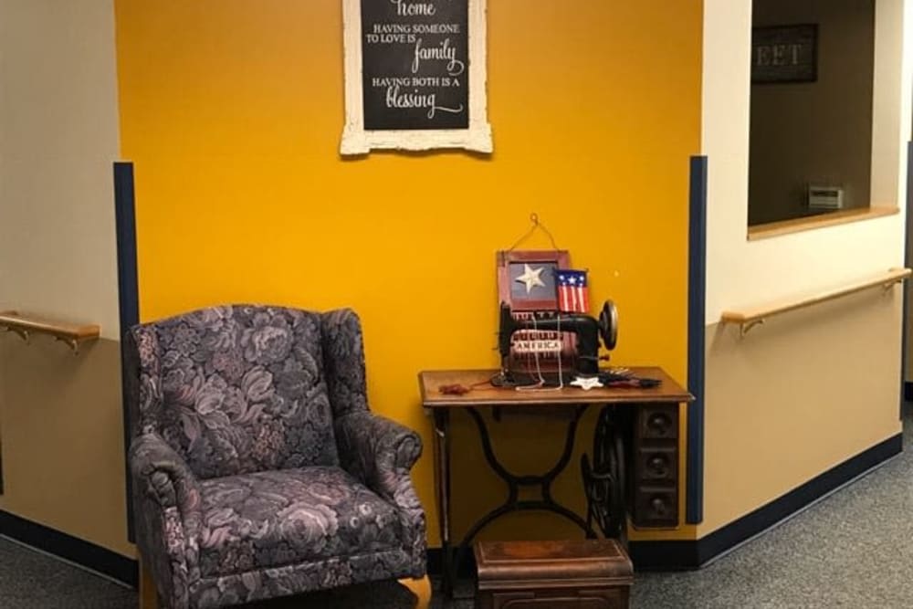 A cozy corner with a vintage armchair and sewing machine against a mustard yellow wall adorned with decor.
