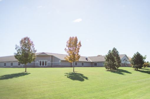 A serene view of a building surrounded by lush green grass and trees on a sunny day.