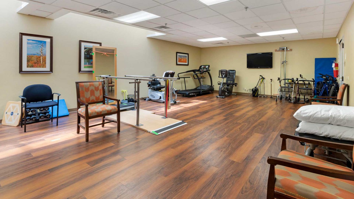 A spacious gym with exercise equipment, featuring a treadmill and wooden flooring.