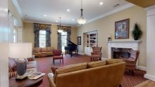 A spacious living room with a grand piano, sofas, chairs, and a fireplace.
