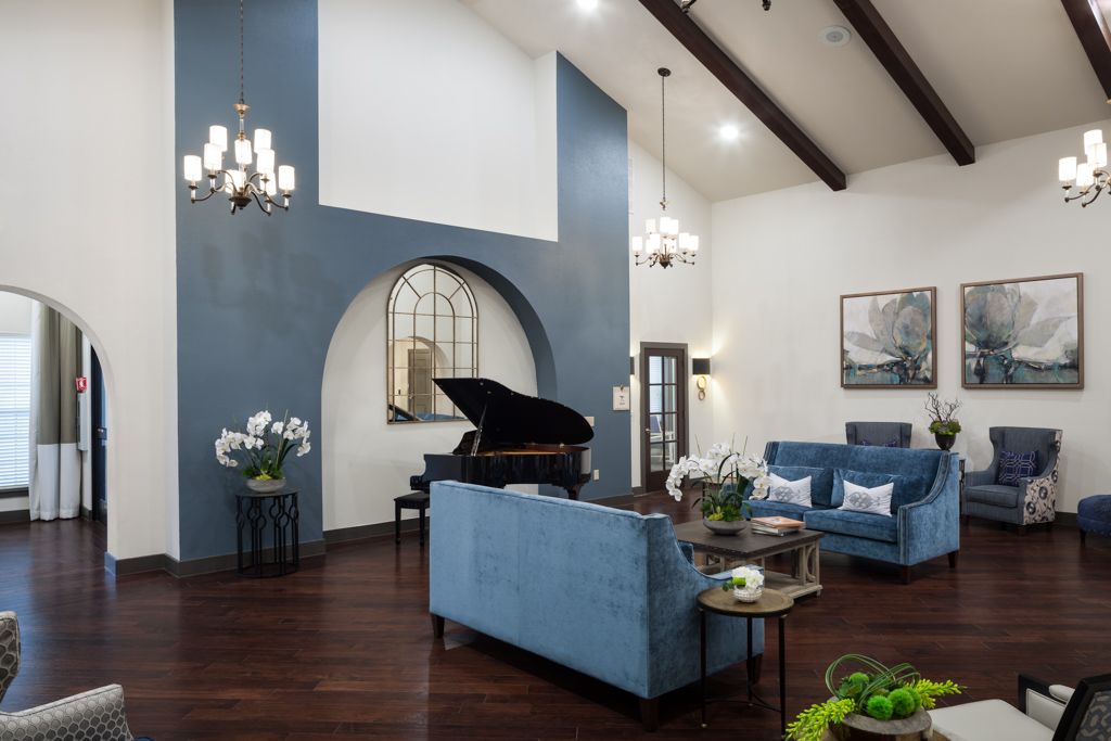Stylish living room featuring a grand piano and blue furniture, highlighted by elegant chandeliers and a beamed ceiling.