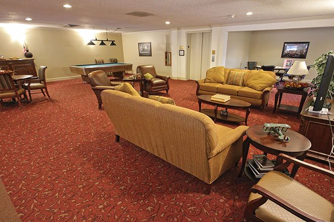 A cozy lounge area with sofas, chairs, and a coffee table on a red carpeted floor.