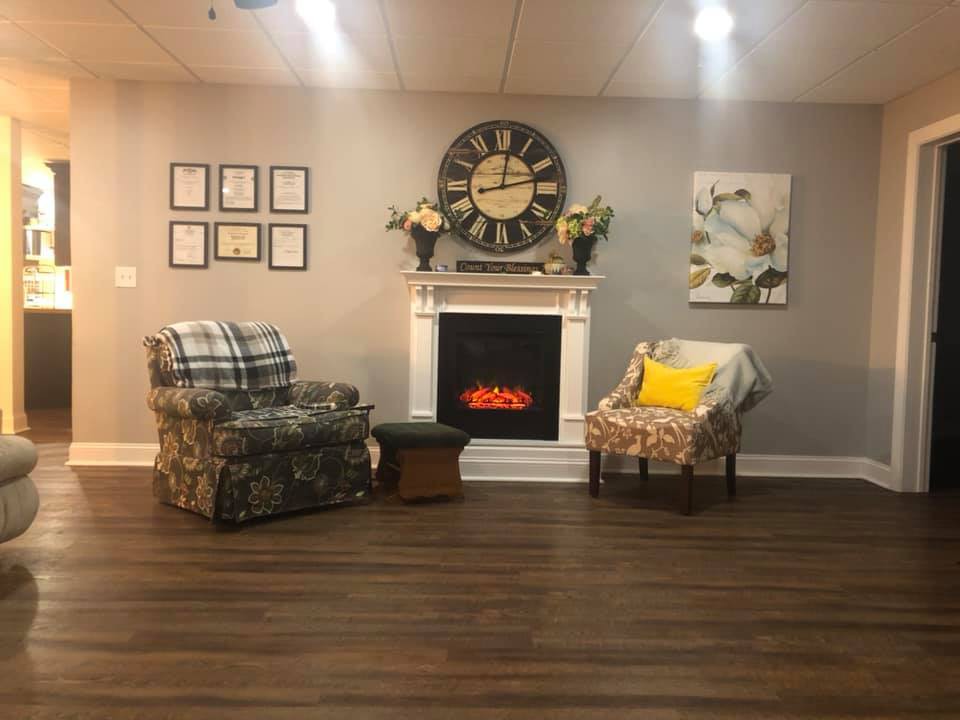 A cozy living room setup featuring armchairs, a decorative fireplace, and a large wall clock.