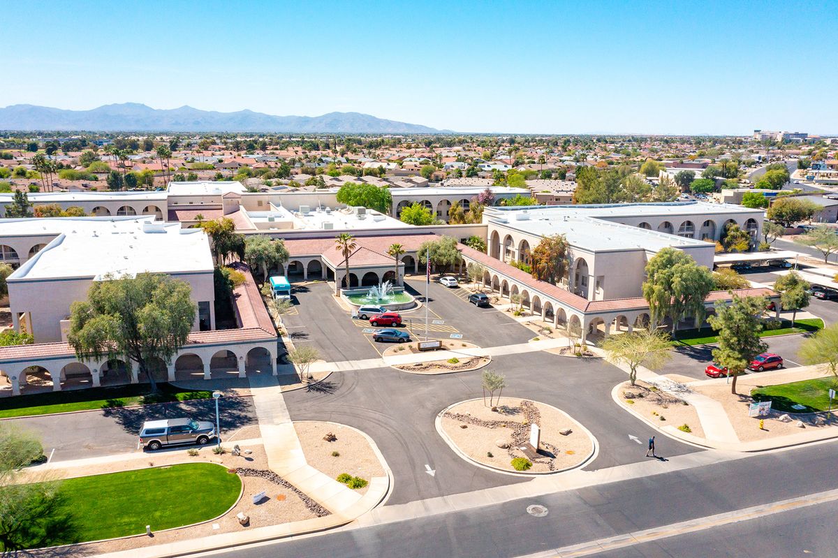 Aerial view of a shopping center with parking lots surrounded by desert landscape and mountains in the distance.