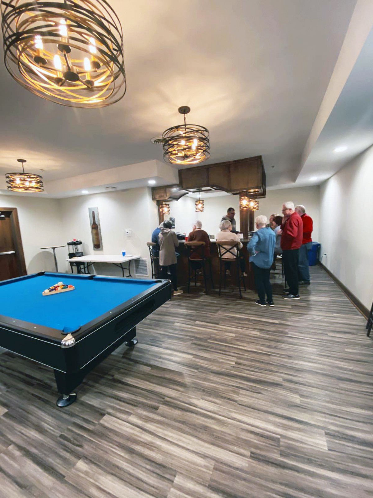 A group of people socializing in a game room with a pool table and bar area.