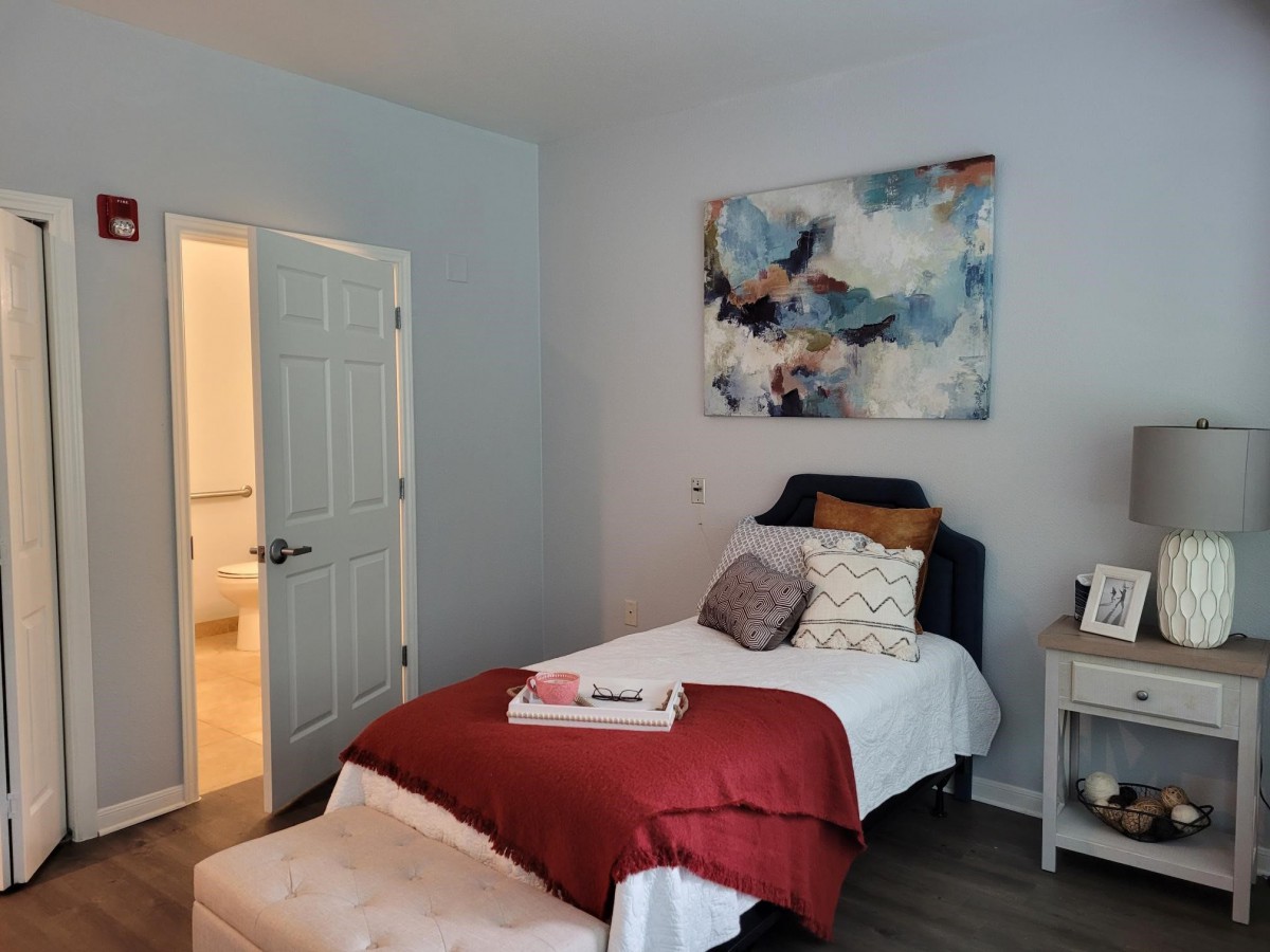 A cozy bedroom with a single bed featuring decorative pillows and a red throw blanket, complemented by abstract artwork on the wall.