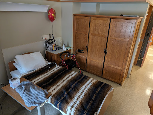 A view of a hospital patient room featuring a bed with a striped blanket and a wooden wardrobe.