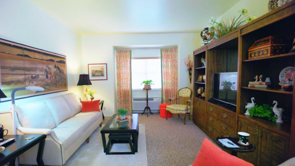 A cozy living room with a sofa, TV stand, and coffee table, featuring decorative touches and natural light from the window.