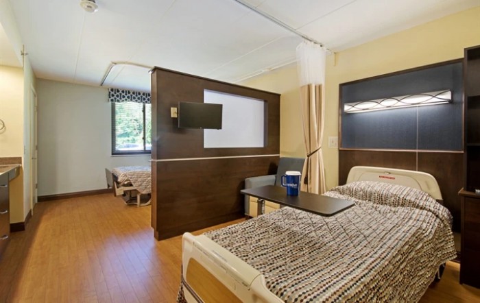 A modern hospital room with patient beds and a privacy curtain, featuring a television for comfort.